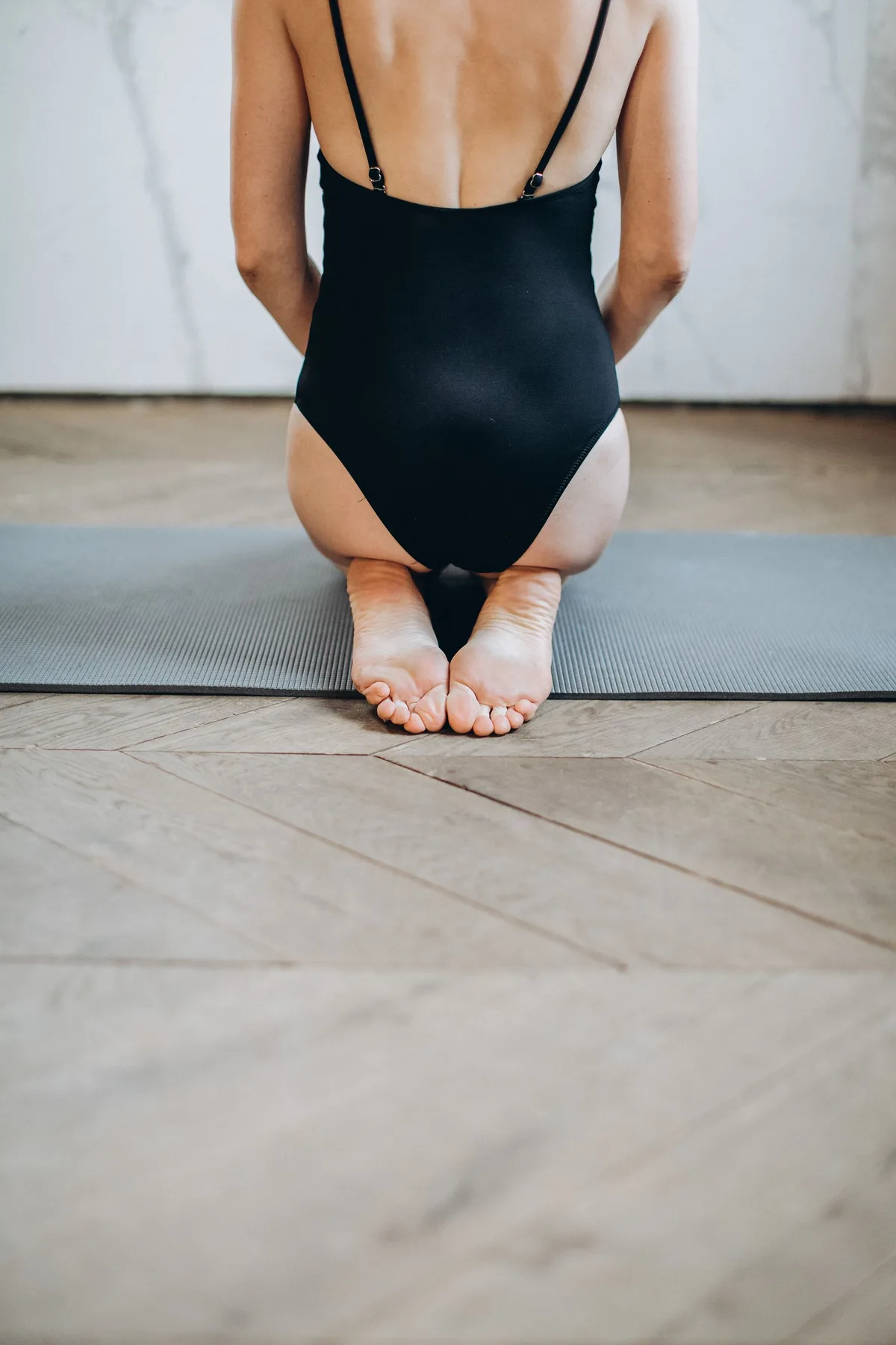 Pratiquante assise sur les talons, de dos, sur un tapis