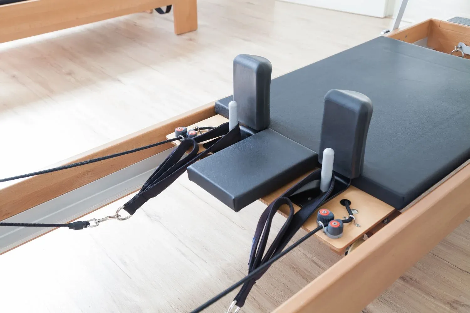 Chariot d’un Reformer en gros plan : appuis d’épaules, sangles et ressorts, sur parquet clair