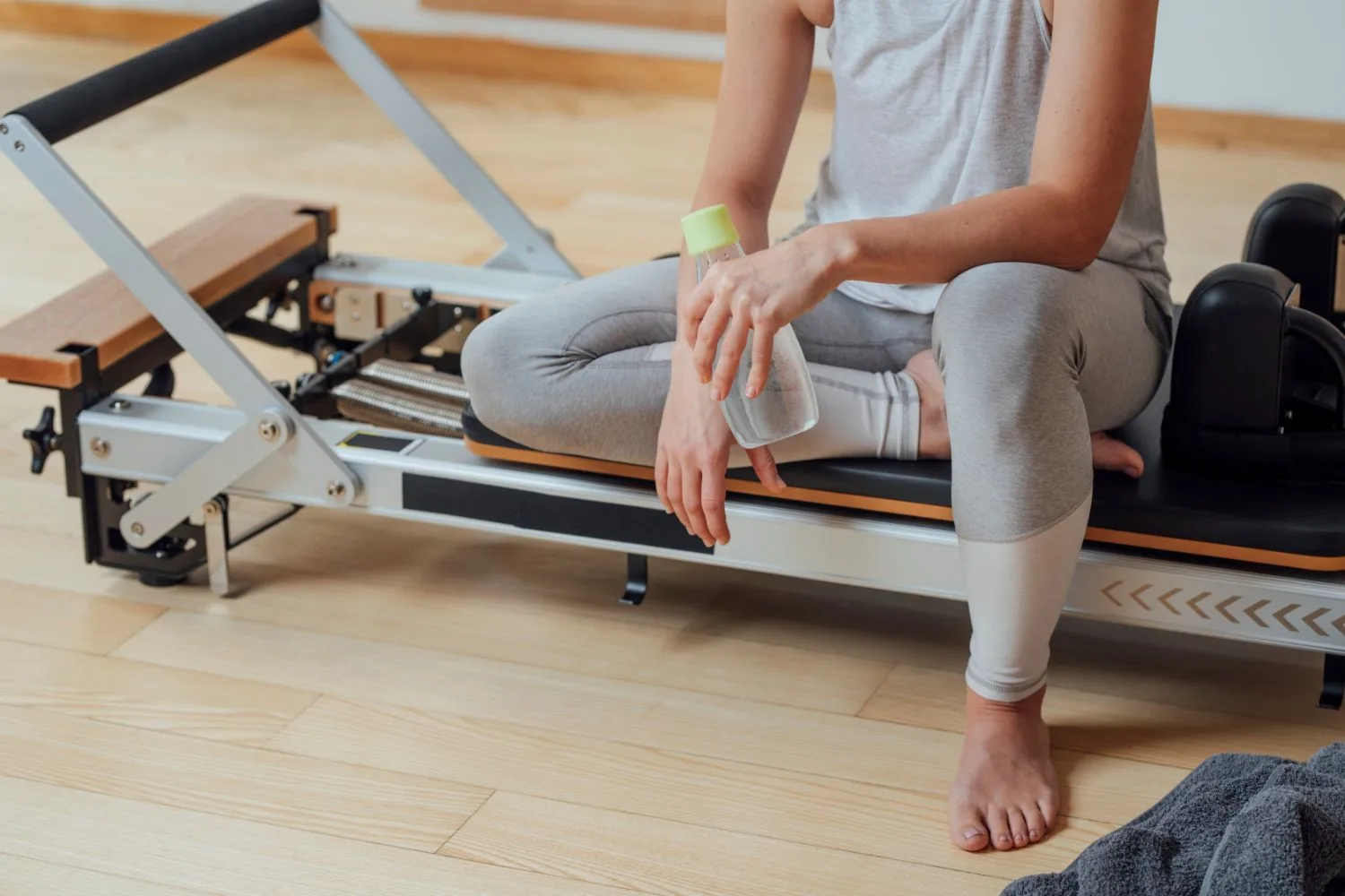 Pratiquante assise sur le chariot d’un Reformer, une gourde à la main, pendant une pause