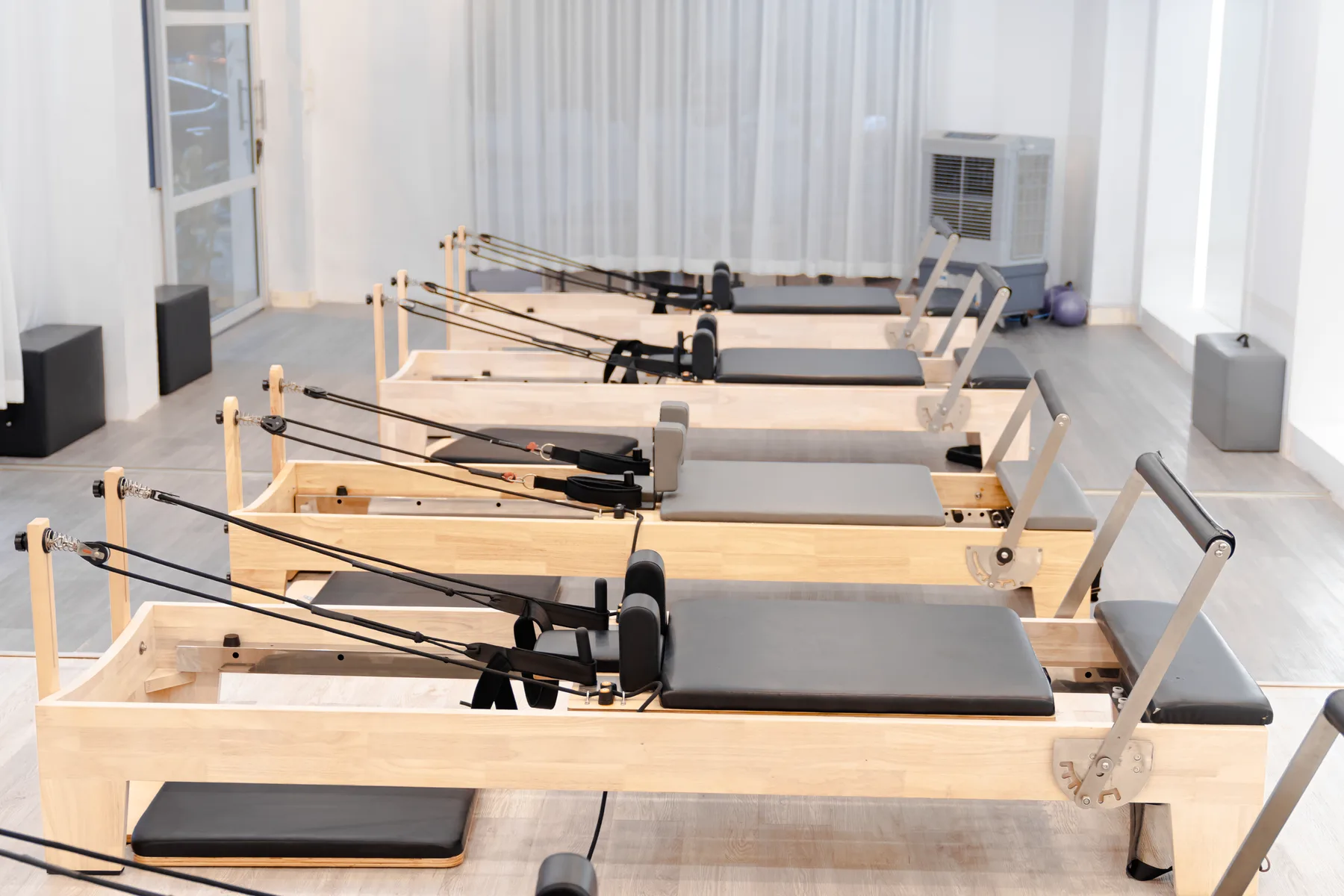 Rangée de Reformers en bois clair et sellerie noire dans une salle lumineuse