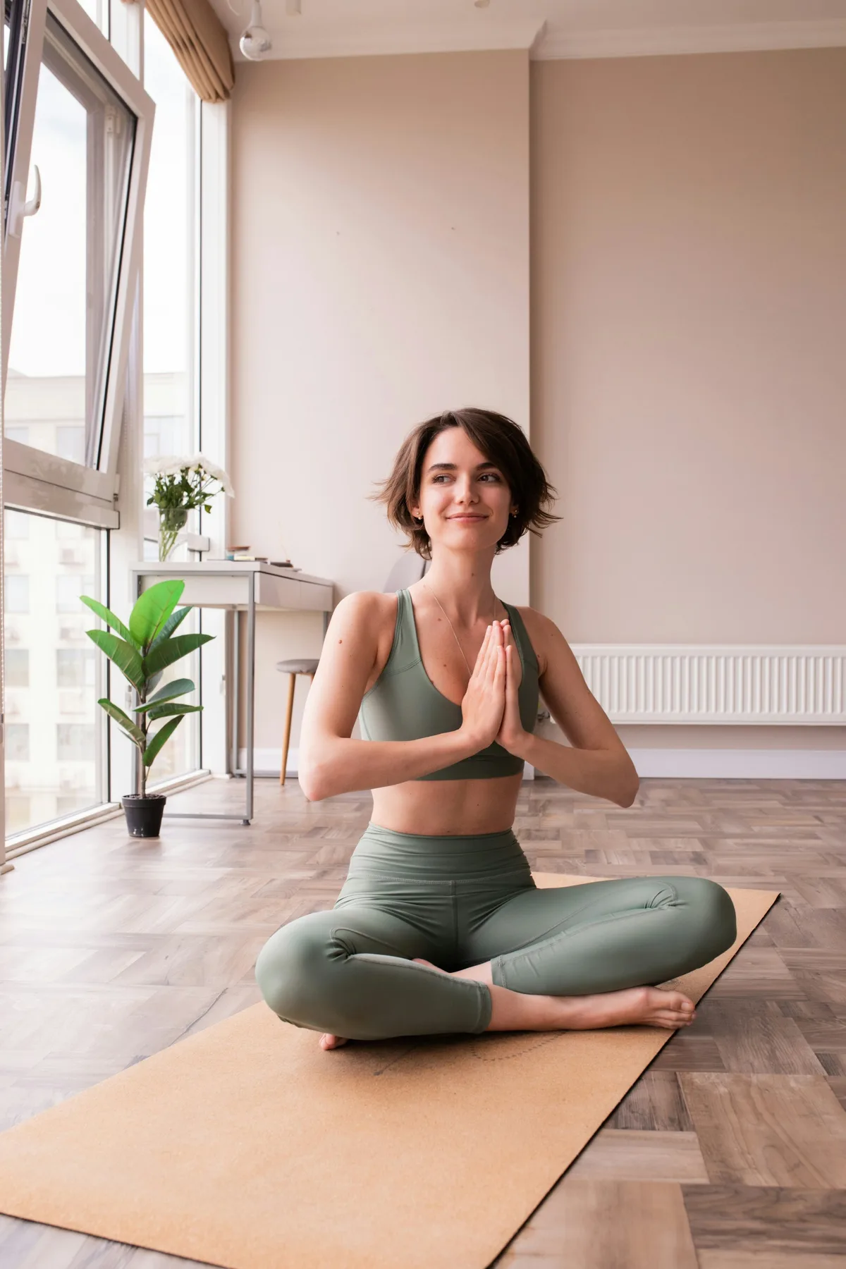 Femme assise en tailleur sur un tapis, mains jointes, en respiration calme
