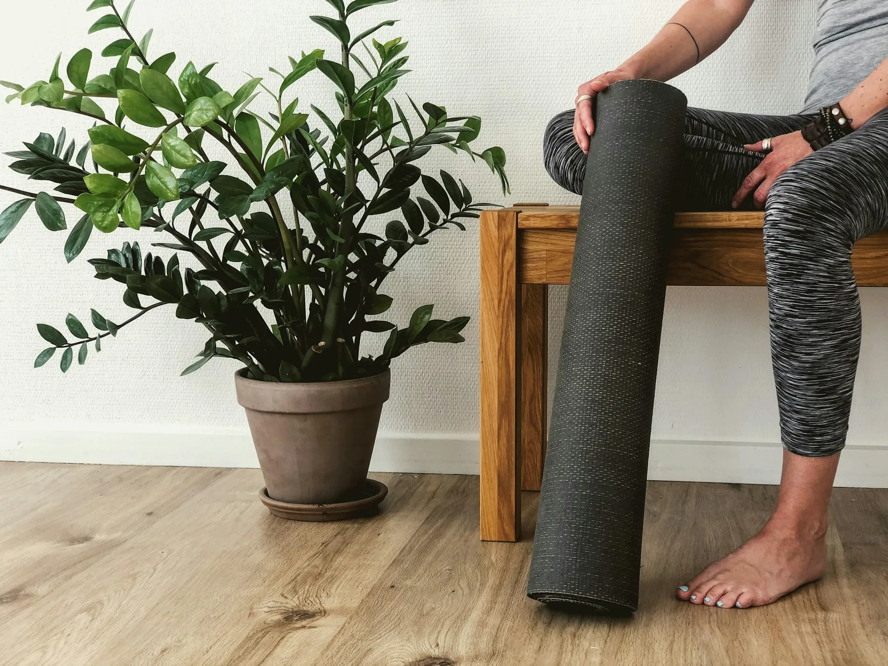 Tapis roulé tenu près d’une plante, pieds nus sur parquet