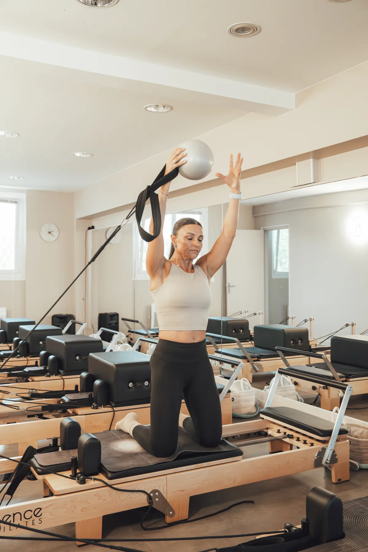 Gaëlle Goffard à genoux sur un Reformer, ballon levé, dans la salle aux huit Reformers