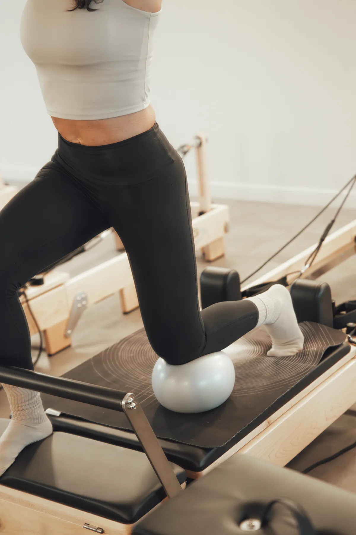 Genoux posés sur le chariot du Reformer, ballon maintenu entre les jambes